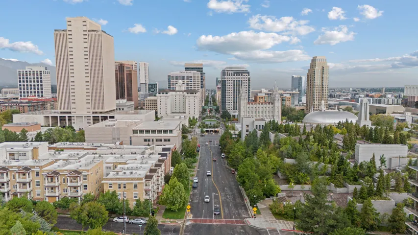 Aerial perspective showcasing a vibrant urban landscape, diverse architectural styles, prominent tall buildings, abundant green spaces, and a clear sky with scattered clouds