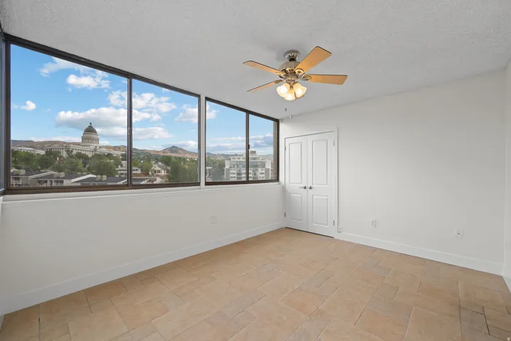 Expansive windows with city and mountain scenery, ceiling fan with integrated lighting, double-door closet, and tile flooring