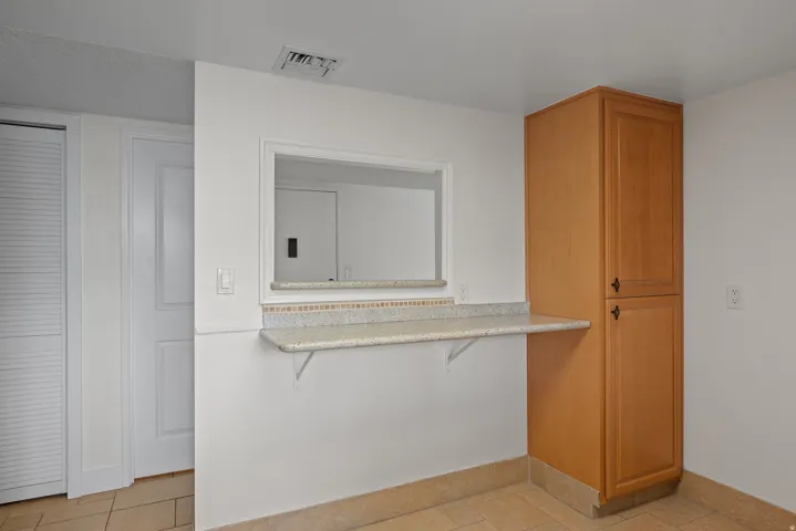 Wood-tone cabinetry with black hardware, pass-through window with an integrated sill, granite countertop, and tile flooring