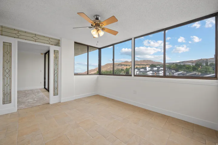 Travertine tile flooring, expansive windows, decorative glass partition, ceiling fan with integrated lighting, mountain scenery