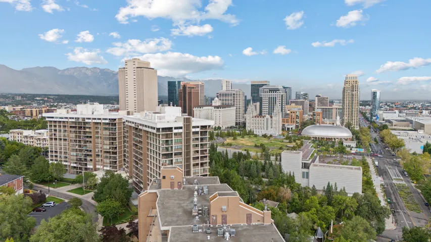 Aerial perspective featuring a vibrant urban landscape, prominent downtown skyline, expansive green spaces, and distant mountain ranges