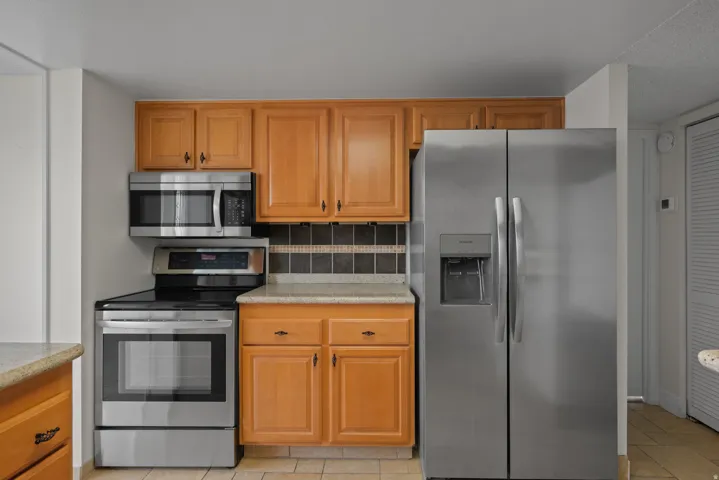 Stainless steel appliances, wood cabinetry, tile backsplash, and light-toned countertops