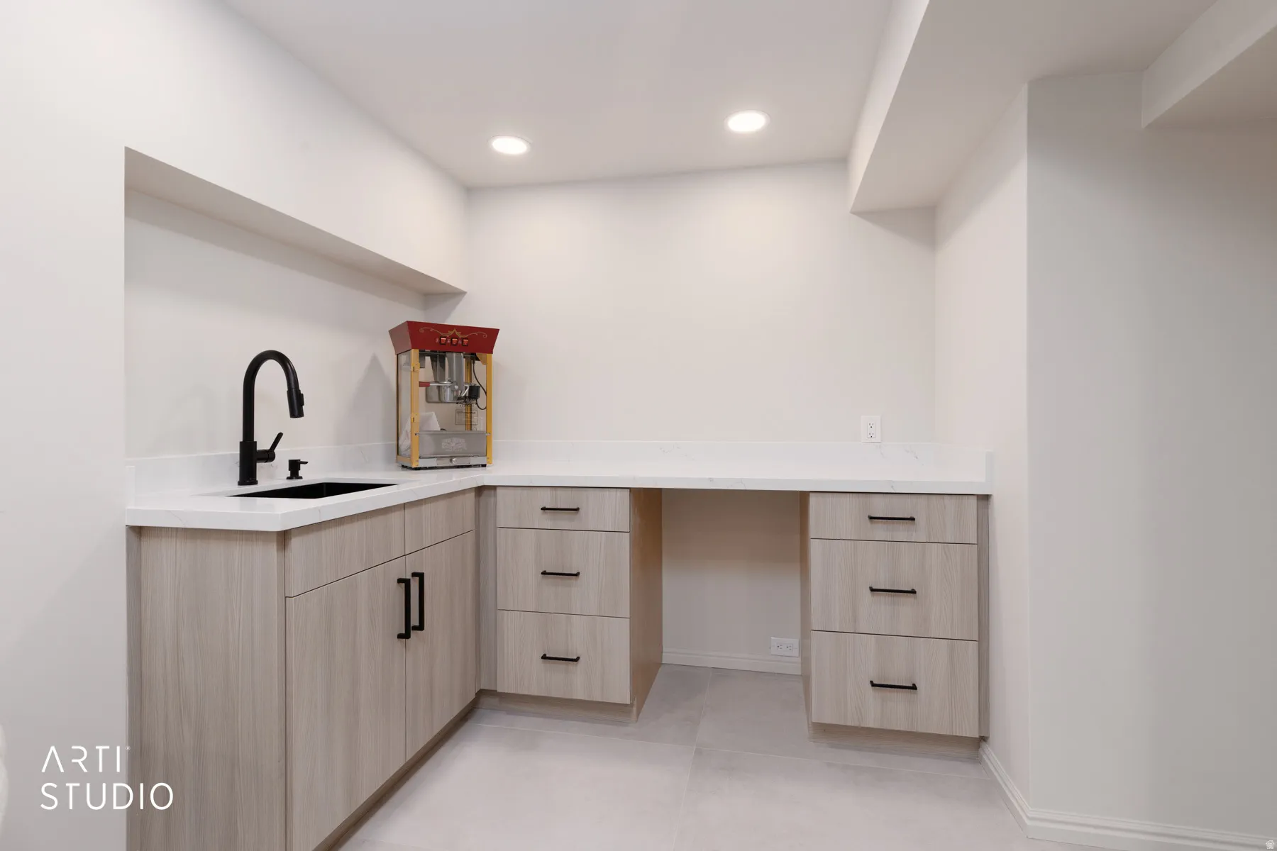 Built-in cabinetry with light wood-finish doors and drawers, a black sink, a black gooseneck faucet, and white countertops