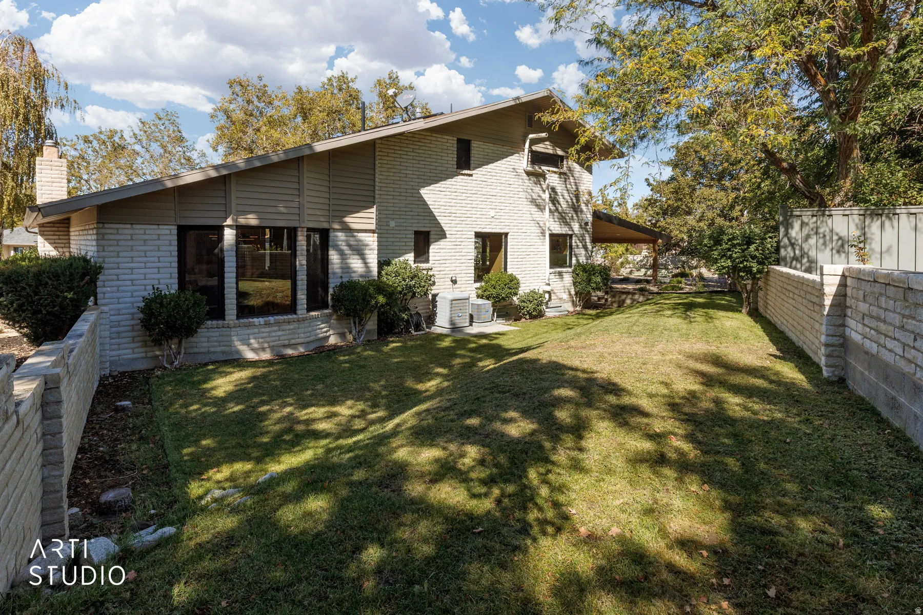 Expansive rear yard featuring a manicured lawn, brick retaining wall, and mature perimeter trees