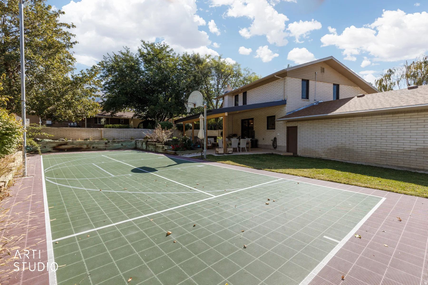 Full-size sports court with a basketball hoop, covered patio, and brick exterior