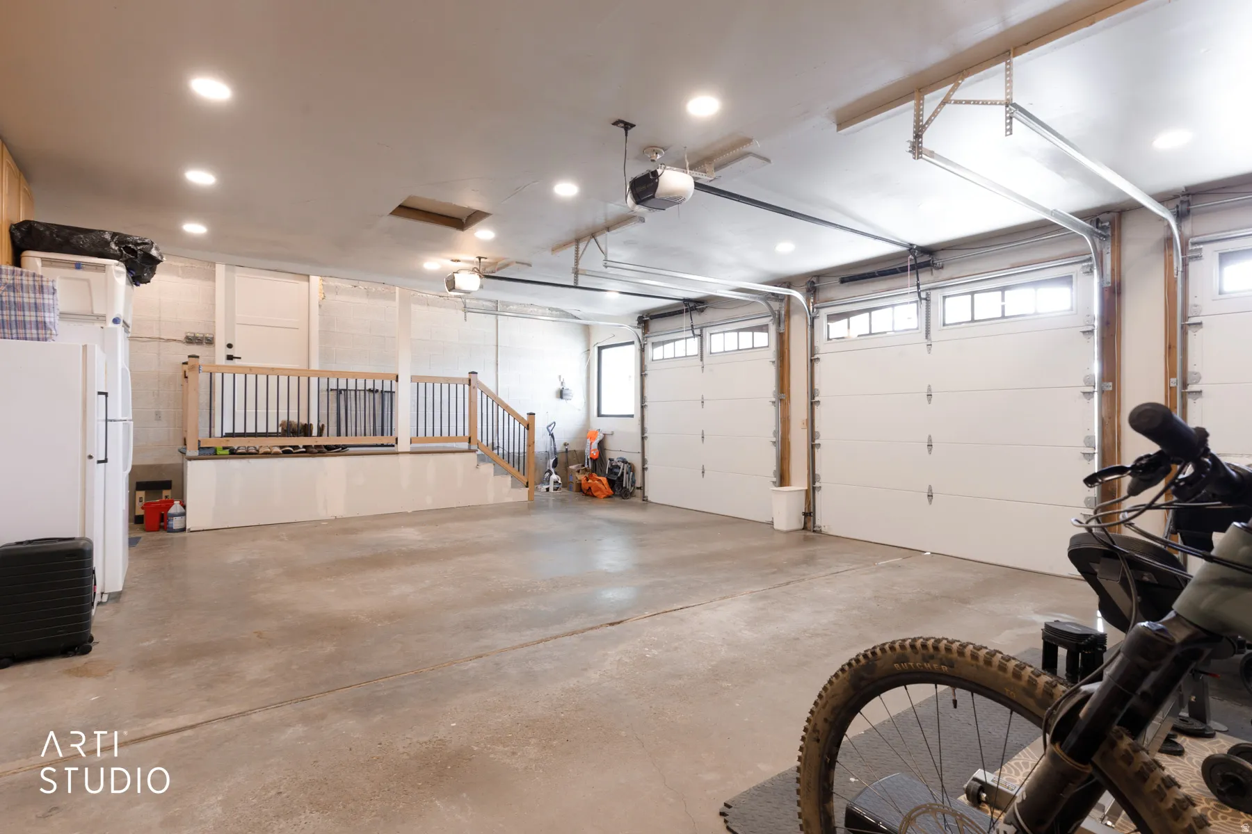 Expansive garage with concrete flooring, two overhead doors with window panels, automatic garage door openers, and recessed lighting