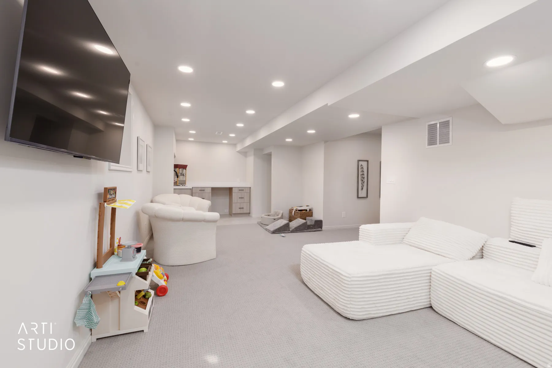 Recessed lighting throughout, light gray wall-to-wall carpeting, built-in desk with lower cabinetry