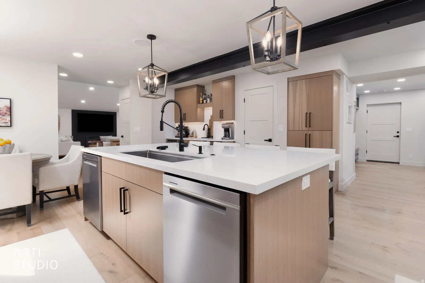 Kitchen island with a white countertop and integrated stainless steel dishwasher, illuminated by two geometric pendant lights