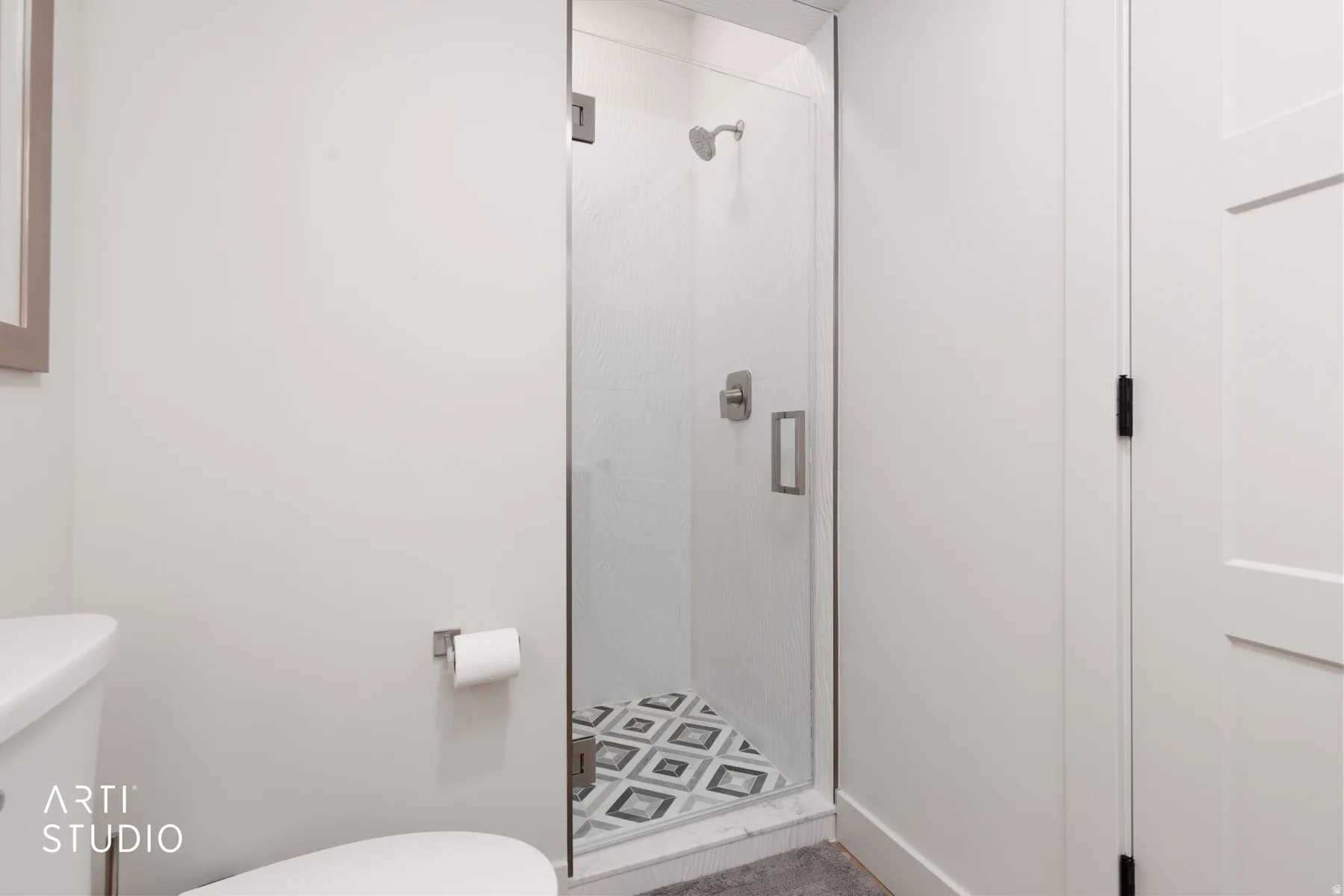 Glass-enclosed shower with a patterned tile floor, brushed nickel shower fixtures, and a white paneled door