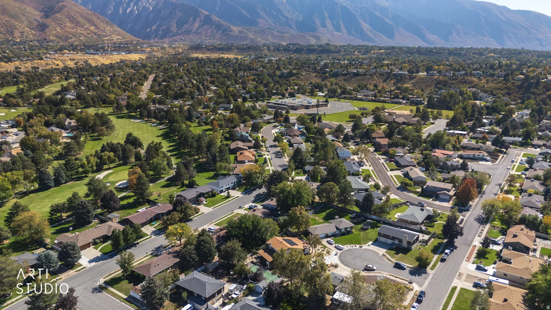 Expansive residential area with mature trees, mountain backdrop, and a nearby golf course