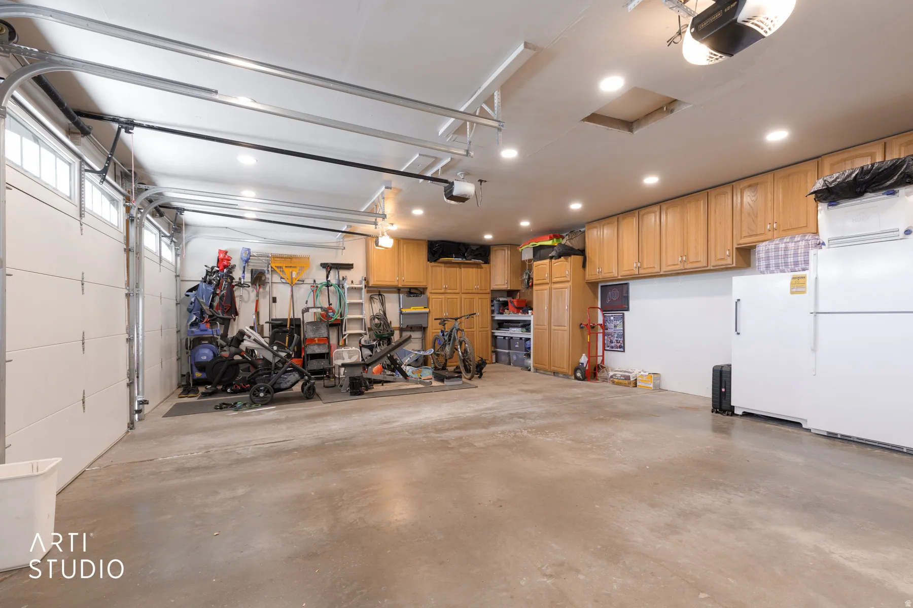 Attached garage with concrete flooring, recessed lighting, white panel garage doors, and built-in wood-finish cabinetry