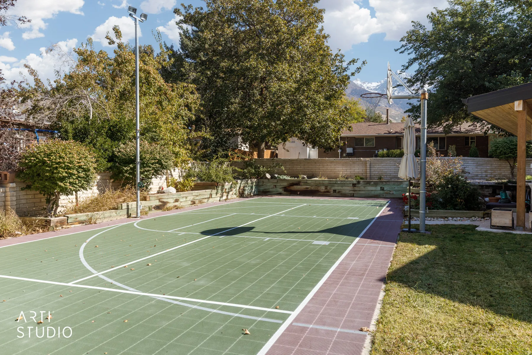 Outdoor sport court with painted lines, integrated basketball hoop, and surrounding mature trees