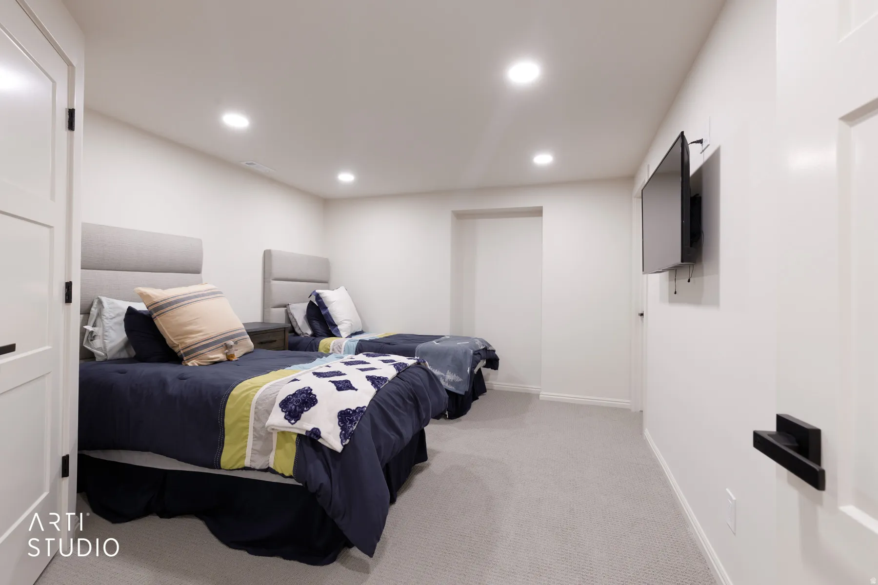 Recessed lighting, wall-mounted television, neutral carpeting, flat panel doors, and contrasting dark hardware