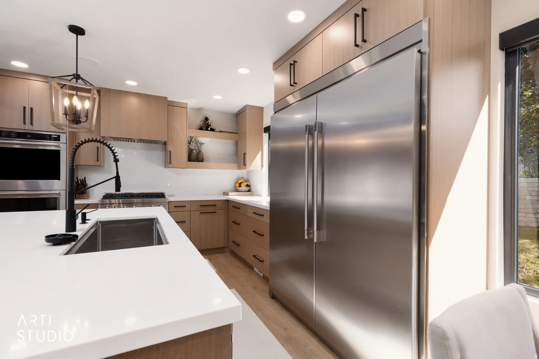 Integrated stainless steel refrigerator, white countertops, wood-finish cabinetry, stainless steel double ovens, and a matte black faucet