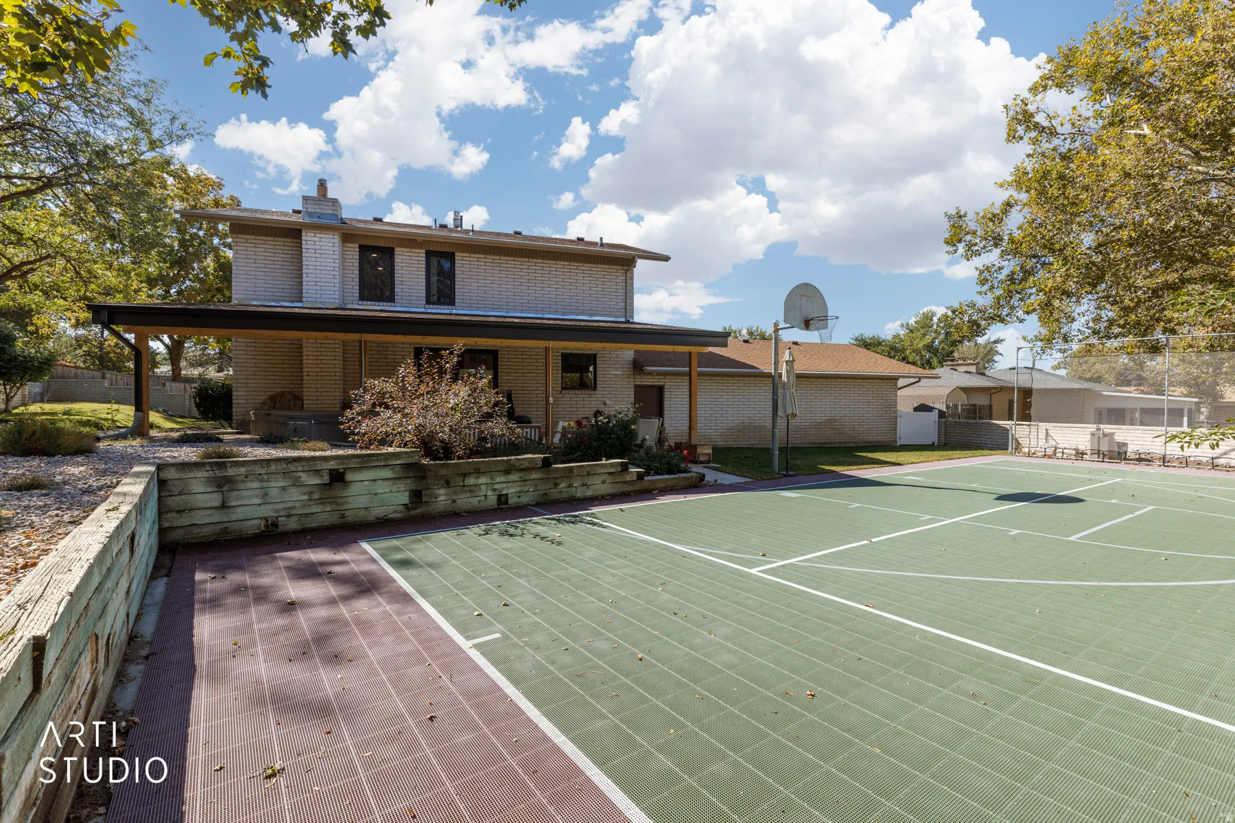 Brick exterior with a covered patio, featuring a built-in basketball hoop, and a sport court with marked lines