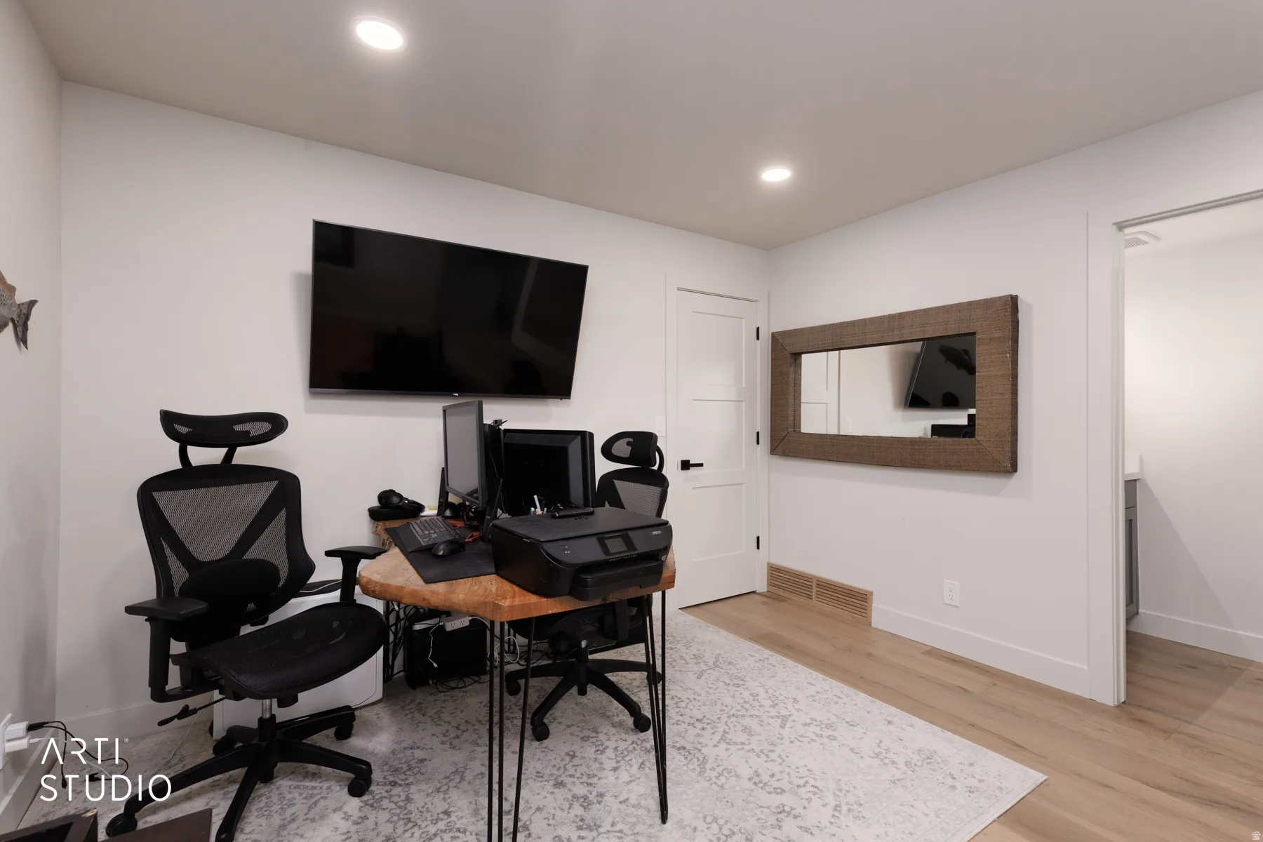 Recessed ceiling lighting, light wood-finish flooring, white walls, and a white interior door with black hardware