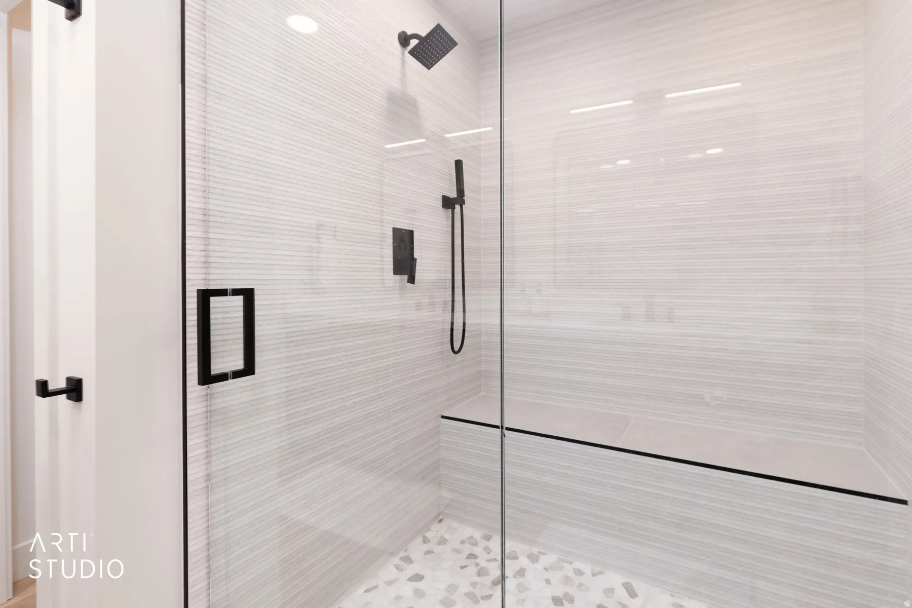 Walk-in shower with clear glass enclosure, matte black fixtures, stone pebble flooring, integrated bench, and textured wall tiling