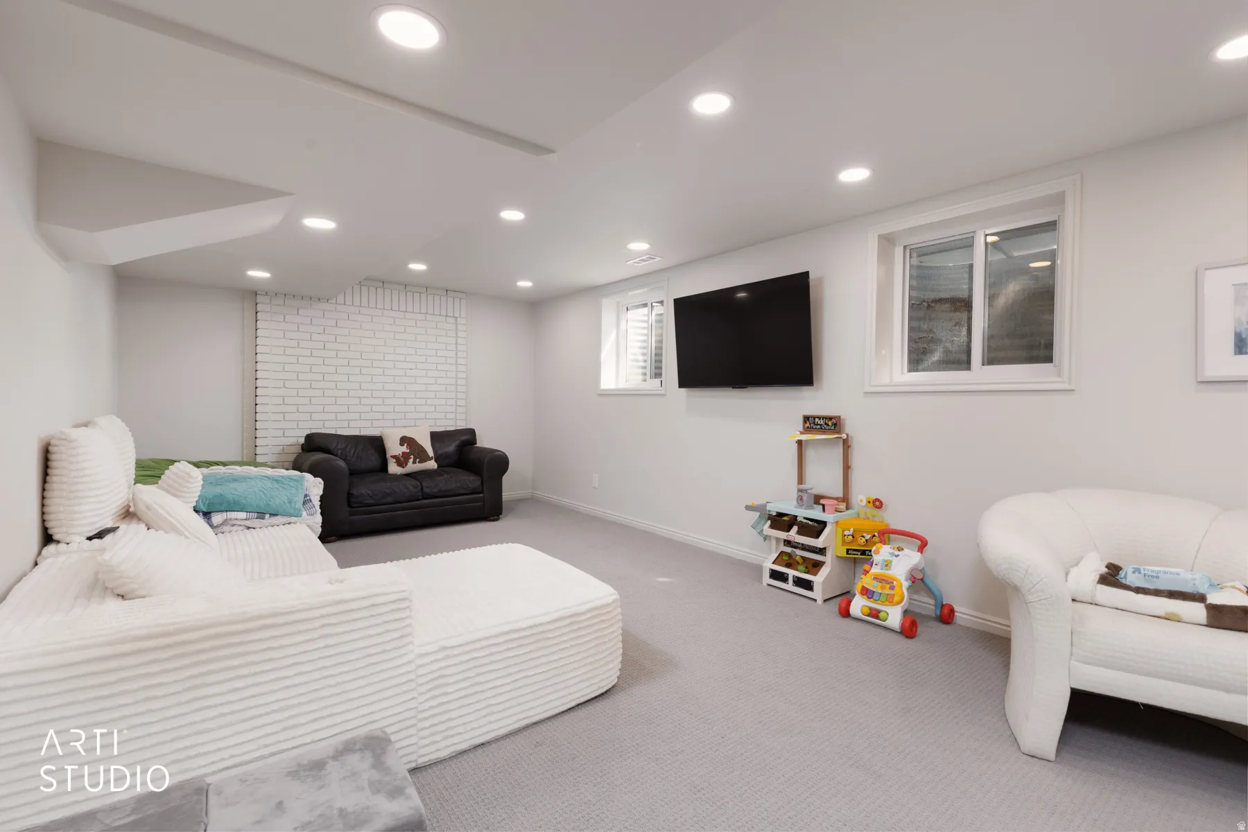 Recessed lighting, light-colored carpeting, white painted brick accent wall, and multiple windows