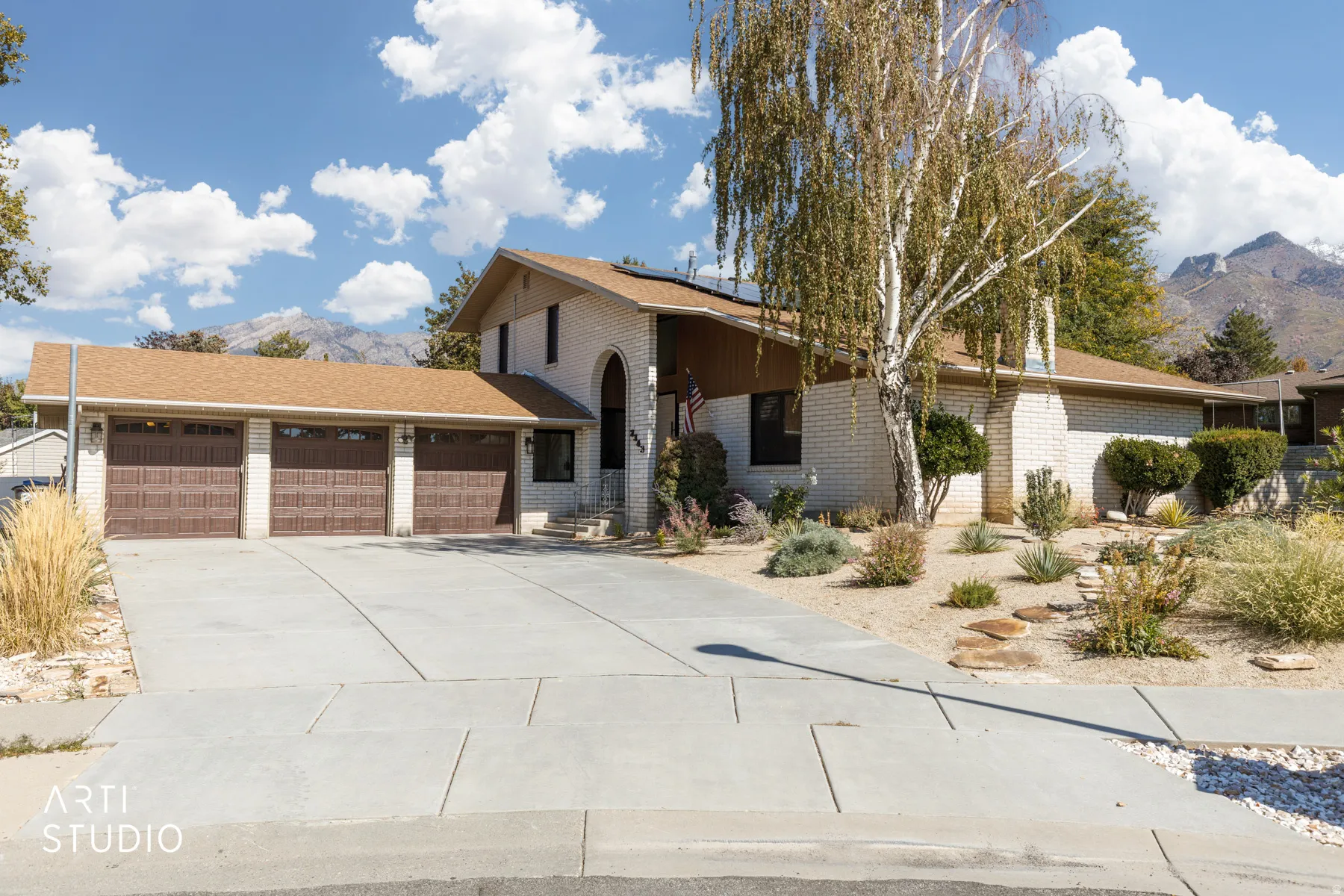 Light-colored brick exterior with an arched entryway, three-car garage, and a concrete driveway