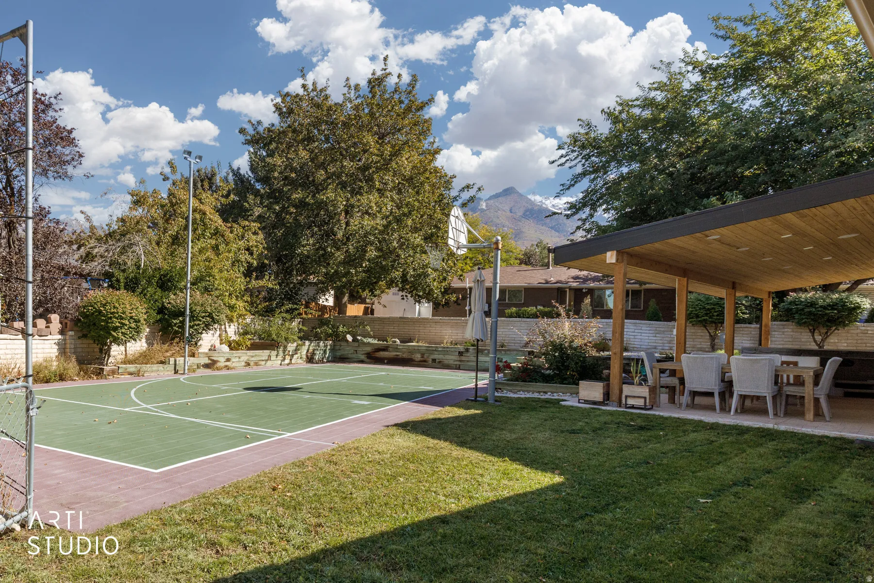 Expansive backyard with a built-in sports court, covered patio with wood-finish ceiling, and mature trees