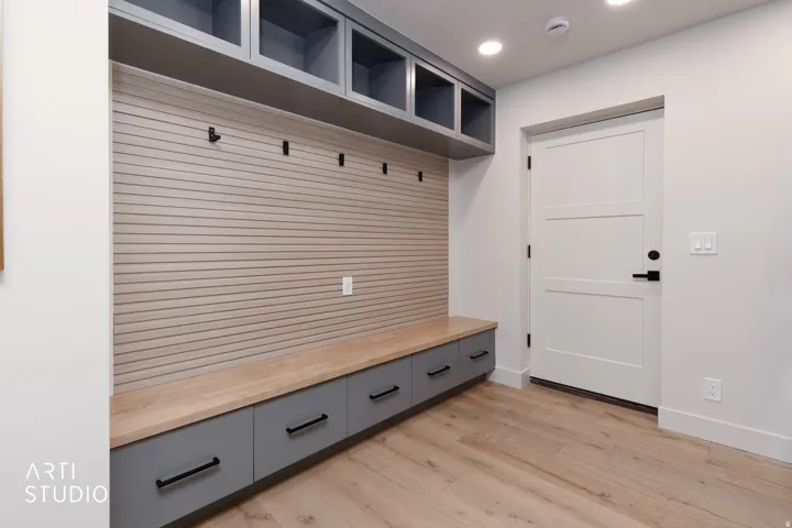 Built-in storage bench with gray cabinetry, wood-finish countertop, and integrated hooks