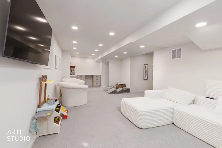 Recessed lighting throughout, light gray wall-to-wall carpeting, built-in desk with lower cabinetry