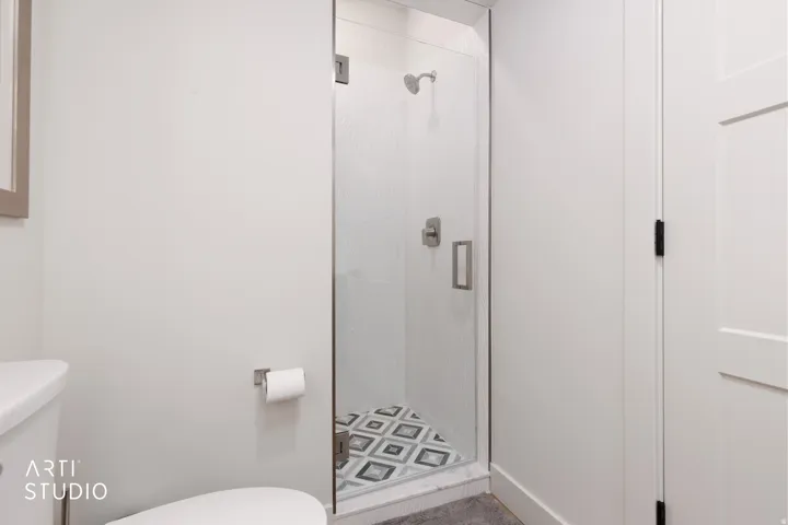 Glass-enclosed shower with a patterned tile floor, brushed nickel shower fixtures, and a white paneled door