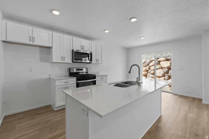 Bright kitchen featuring white cabinetry, a large center island with a double basin sink, stainless steel appliances, and wood-finish flooring