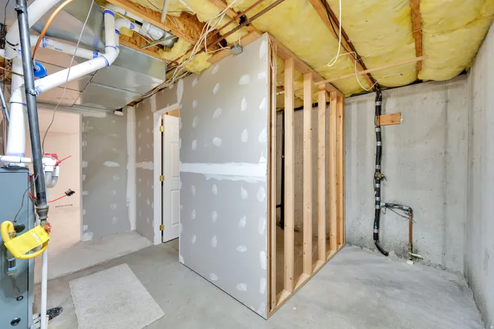 Unfinished basement with exposed ceiling insulation, wood framing, concrete flooring, and partial drywall installation