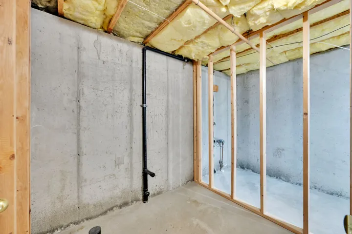 Unfinished basement space featuring exposed concrete walls and flooring, wood framing, and visible insulation