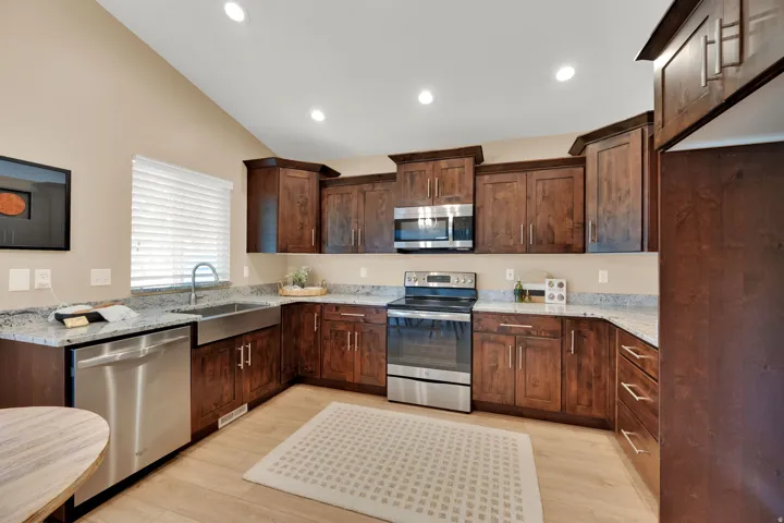 Kitchen featuring wood cabinetry, stainless steel appliances, light-toned wood-finish flooring, recessed lighting, and a vaulted ceiling