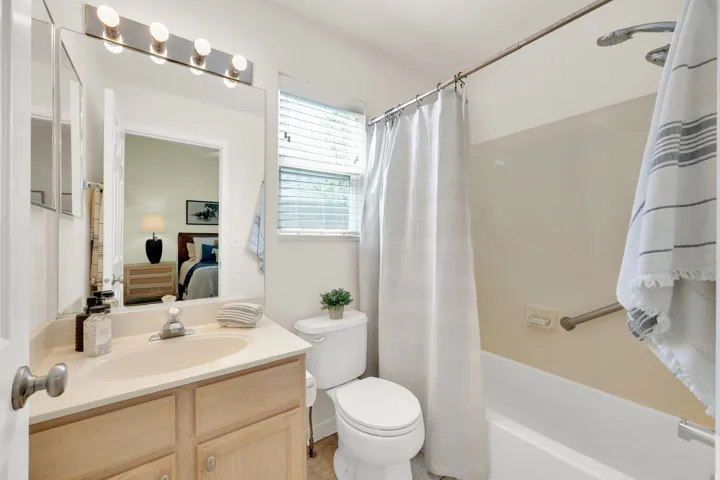 Vanity with a solid surface countertop and undermount sink, built-in tub with a shower fixture, and a window with blinds