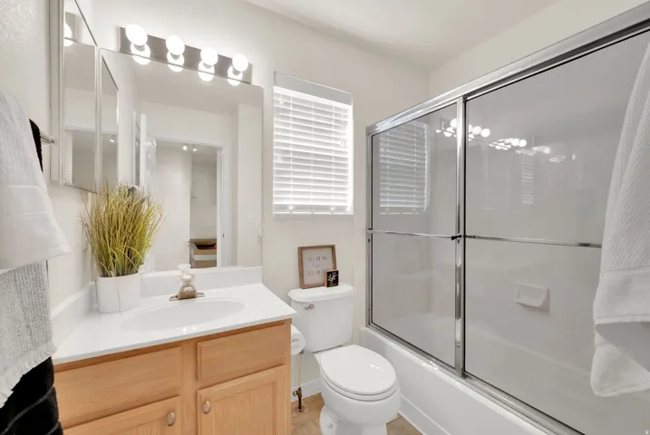 Bathroom featuring a wood-finish vanity with an integrated sink, a frameless wall mirror, and a full bathtub with sliding glass doors