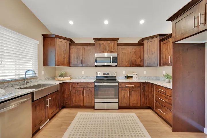 U-shaped kitchen featuring wood-finish cabinetry, stainless steel appliances, a farmhouse sink, light-toned countertops, and recessed lighting