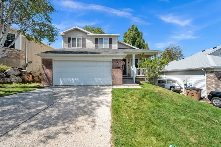 Two-story residence featuring a two-car garage, brick facade accents, a covered entry porch, and a sloped grass lawn