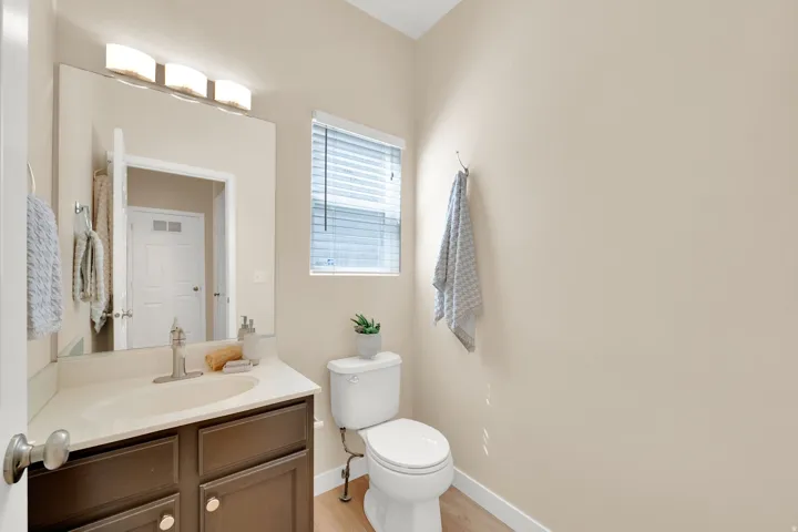 Wood-finish flooring, single-pane window, flush-mounted vanity lighting, dark wood-finish vanity with countertop, and a built-in toilet