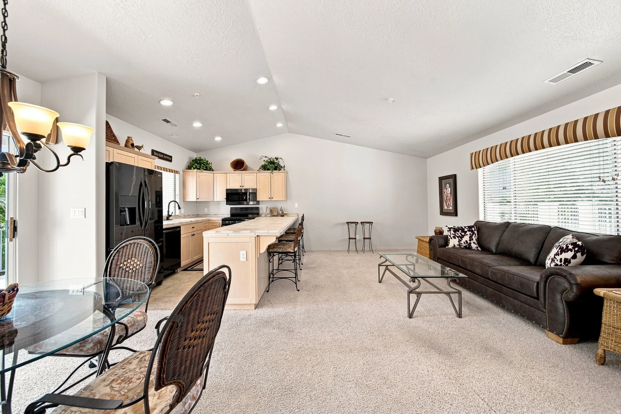 Vaulted ceiling, recessed lighting, kitchen island with seating, black appliances, and neutral carpeting