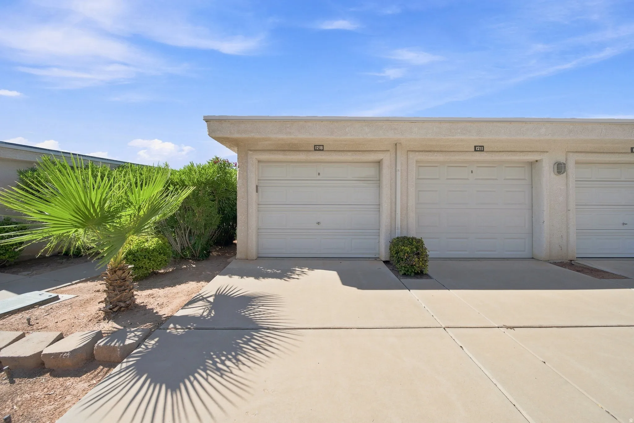 Individual garage doors, exterior wall sconces, concrete driveway, and mature landscaping