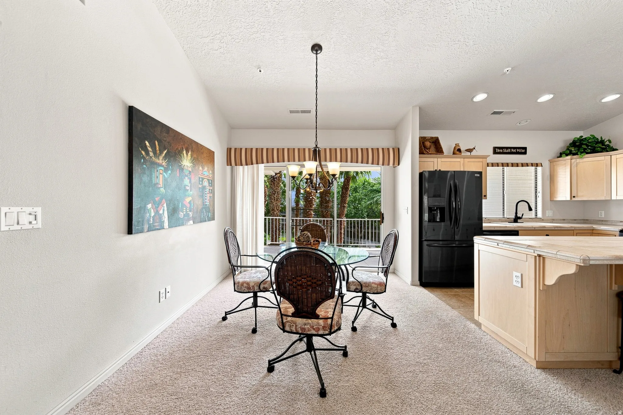 Light carpeted flooring, vaulted ceiling, recessed lighting, double glass sliding doors, and a kitchen featuring wood-finish cabinetry