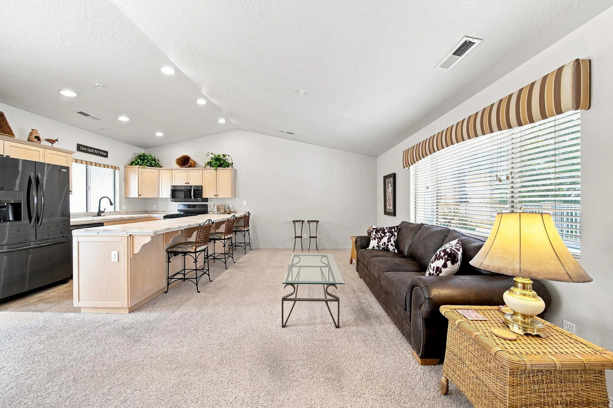 Open concept living area featuring vaulted ceilings, recessed lighting, a kitchen island with seating, a built-in microwave, and a black appliance package