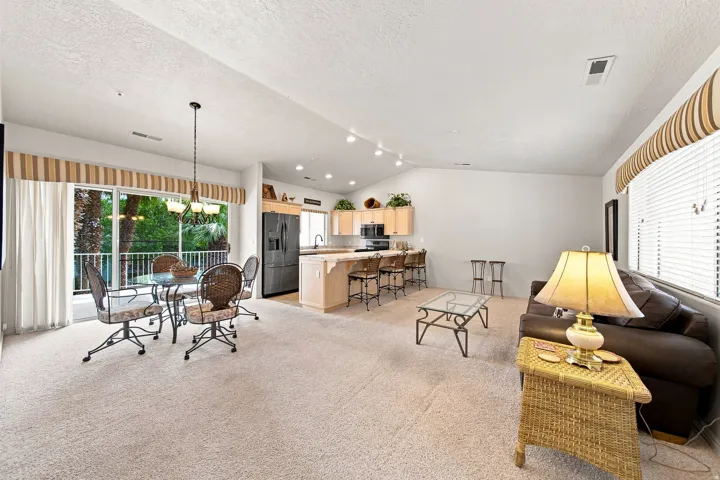 Open-concept living space featuring a dining area, kitchen with breakfast bar, and large windows with blinds