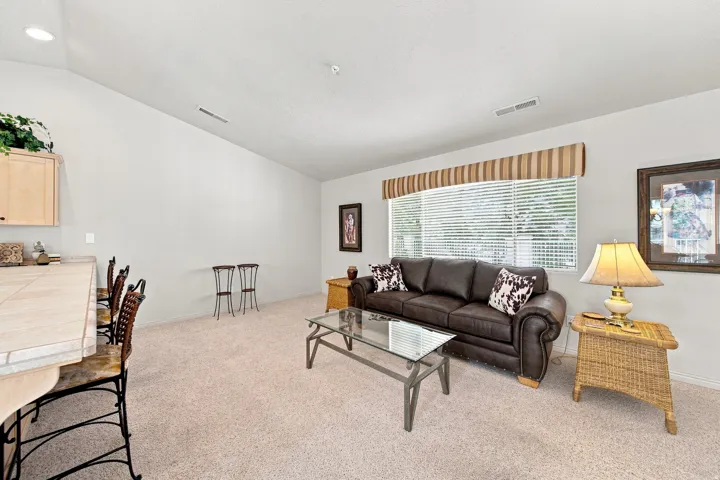 Vaulted ceiling, recessed lighting, expansive window with blinds, and light-toned carpeting