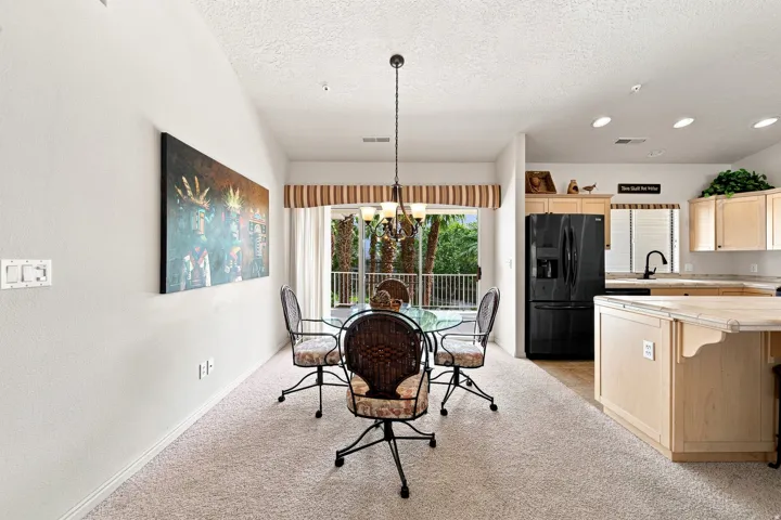 Light carpeted flooring, vaulted ceiling, recessed lighting, double glass sliding doors, and a kitchen featuring wood-finish cabinetry