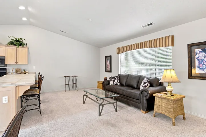 Vaulted ceiling, recessed lighting, neutral carpet, large window with blinds, and a kitchen island with tile countertop