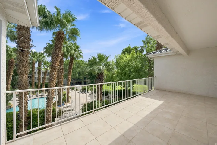 Tiled balcony with a white metal railing overlooking a swimming pool and numerous palm trees
