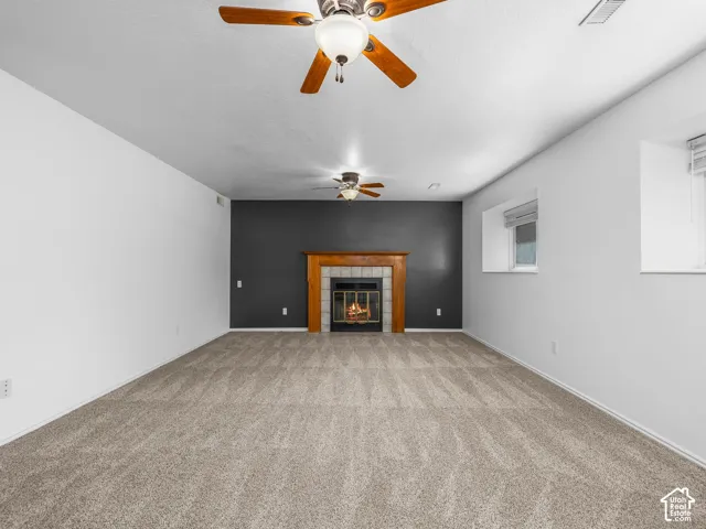 Spacious room with a central fireplace featuring a wood mantel and tile surround, accompanied by two ceiling fans with integrated lighting, and neutral carpeting