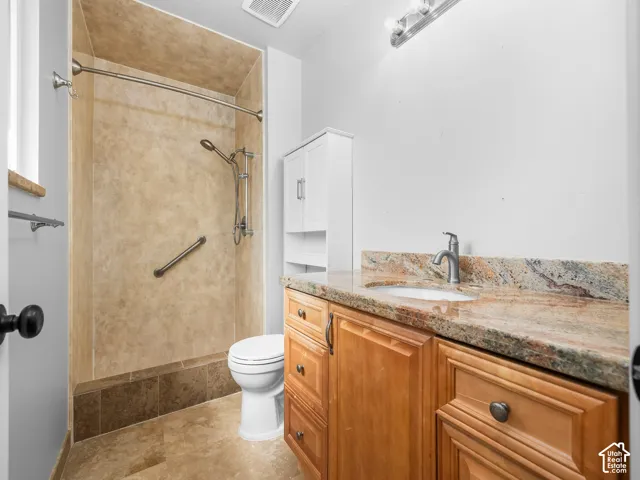 Walk-in shower with grab bar, wood-finish vanity with granite countertop, and white wall cabinet