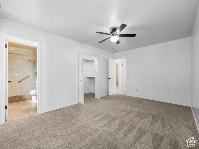Spacious primary bedroom featuring neutral carpeting, ceiling fan with integrated lighting, and direct access to an ensuite bathroom
