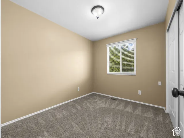 Bright secondary bedroom showcasing neutral taupe walls, neutral carpeting, recessed ceiling lighting, and a large double-hung window with plantation shutters providing natural light and ventilation