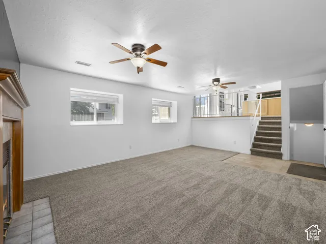 Spacious carpeted area with a wood-mantle fireplace and tile hearth